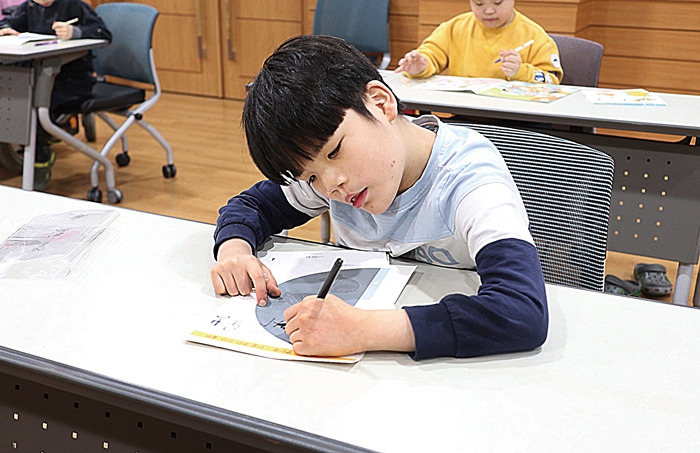 집중하며 연필을 들고 글을 쓰고 있는 장애아동