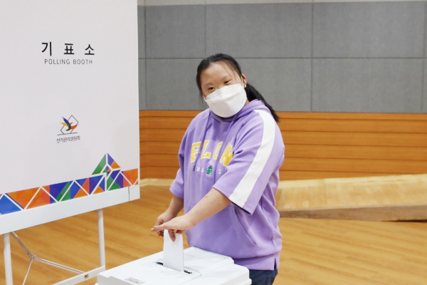 보라색 상의를 입은 여성 장애아동 한 명이 기표를 마친 투표용지를 투표함에 넣고 있는 모습