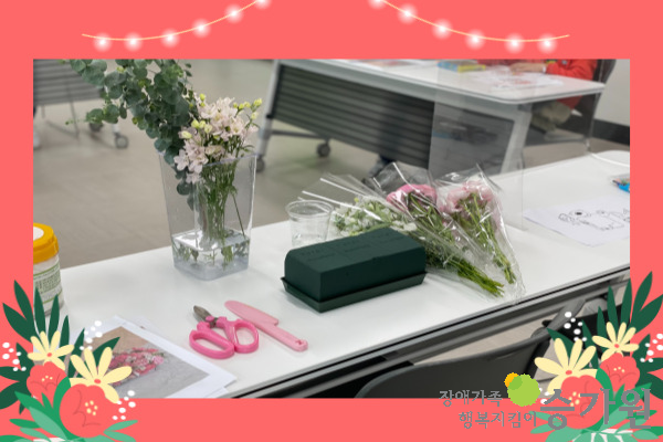 꽃, 가위, 도면 등 꽃꽂이 활동을 하는 데 필요한 준비물들이 책상에 놓여 있다  / 장애가족행복지킴이 승가원ci 삽입