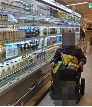 휠체어를 사용하며 쇼핑하는 장애인 당사자의 모습, 음료 매대 앞에서 물건들을 무릎에 쌓은 채 쇼핑하고 있다
