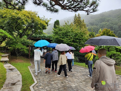 우산을 쓴 약10명의 장애가족과 가족들이 함께 모여 나무가 있는 돌길을 걸어가고 있다. 우측하단 장애가족행복지킴이승가원ci 로고 삽입